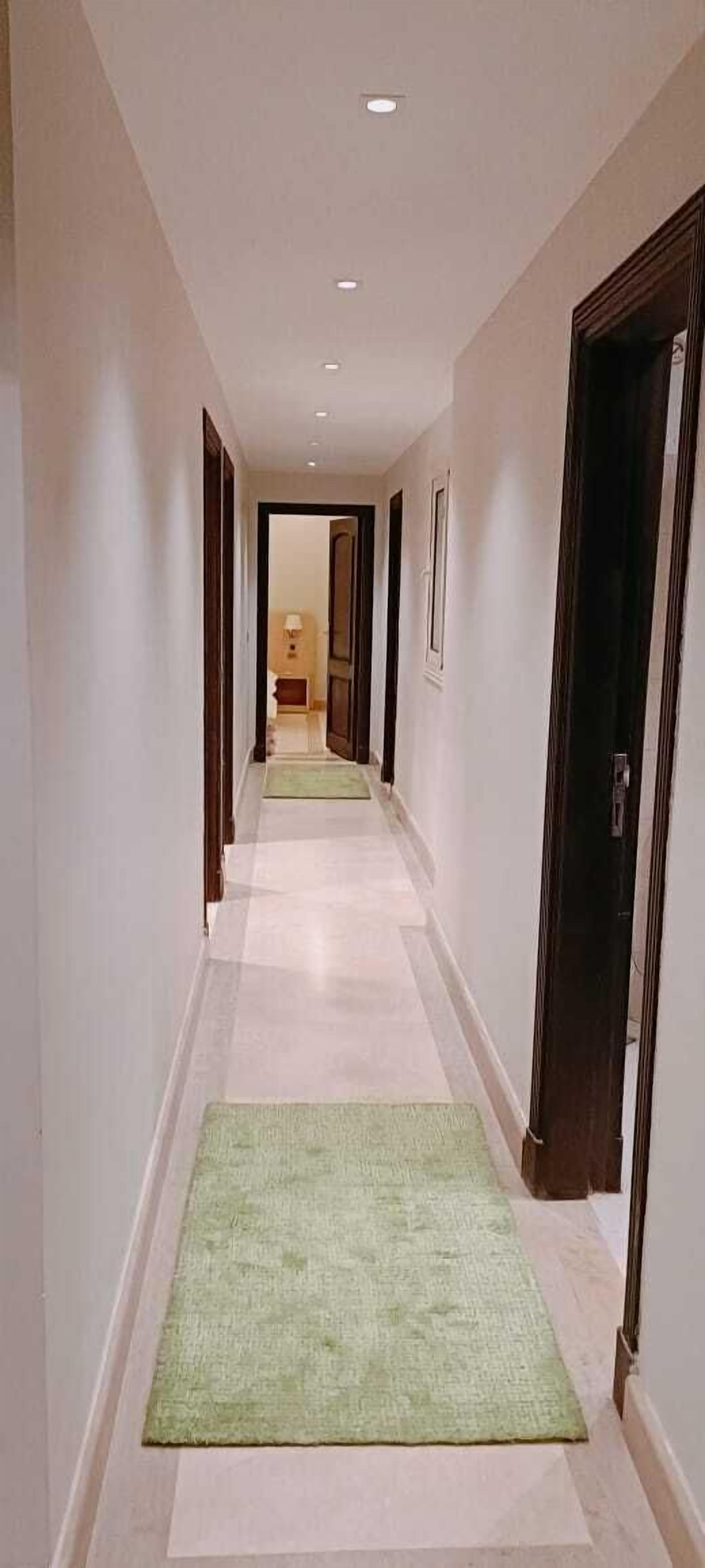 A hallway with a light-colored floor, green rugs, and dark wooden doors.