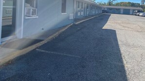 A row of single-story buildings with large windows and air conditioning units, a gravel driveway, and a clear blue sky. - Western Skies Motel (Seagoville)