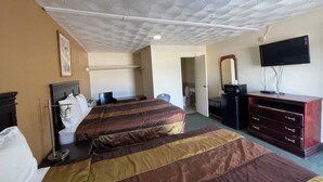 A hotel room with two beds, a desk, a dresser, a television, and a bathroom visible through an open door. - Western Skies Motel (Seagoville)