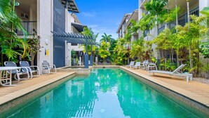 Una piscina con sillones de descanso y una pérgola, rodeada de plantas tropicales.