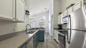 A modern kitchen with stainless steel appliances, a central island, and a view to the dining area. - The Disney & Universal Dog House - Fenced Yard (Davenport)