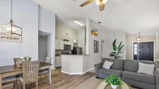 A modern living room with a grey sofa, a dining table with chairs, a kitchen area, and a ceiling fan. - The Disney & Universal Dog House - Fenced Yard (Davenport)