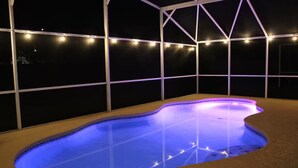 A swimming pool with a curved edge, surrounded by a white metal structure and string lights. - The Disney & Universal Dog House - Fenced Yard (Davenport)