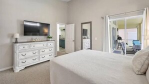 A bedroom with a bed, a dresser, a TV, and a sliding glass door leading to a balcony. - The Disney & Universal Dog House - Fenced Yard (Davenport)