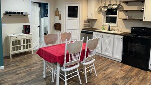 Una cocina compacta con armarios blancos, una mesa de comedor con mantel rojo y una estufa negra.