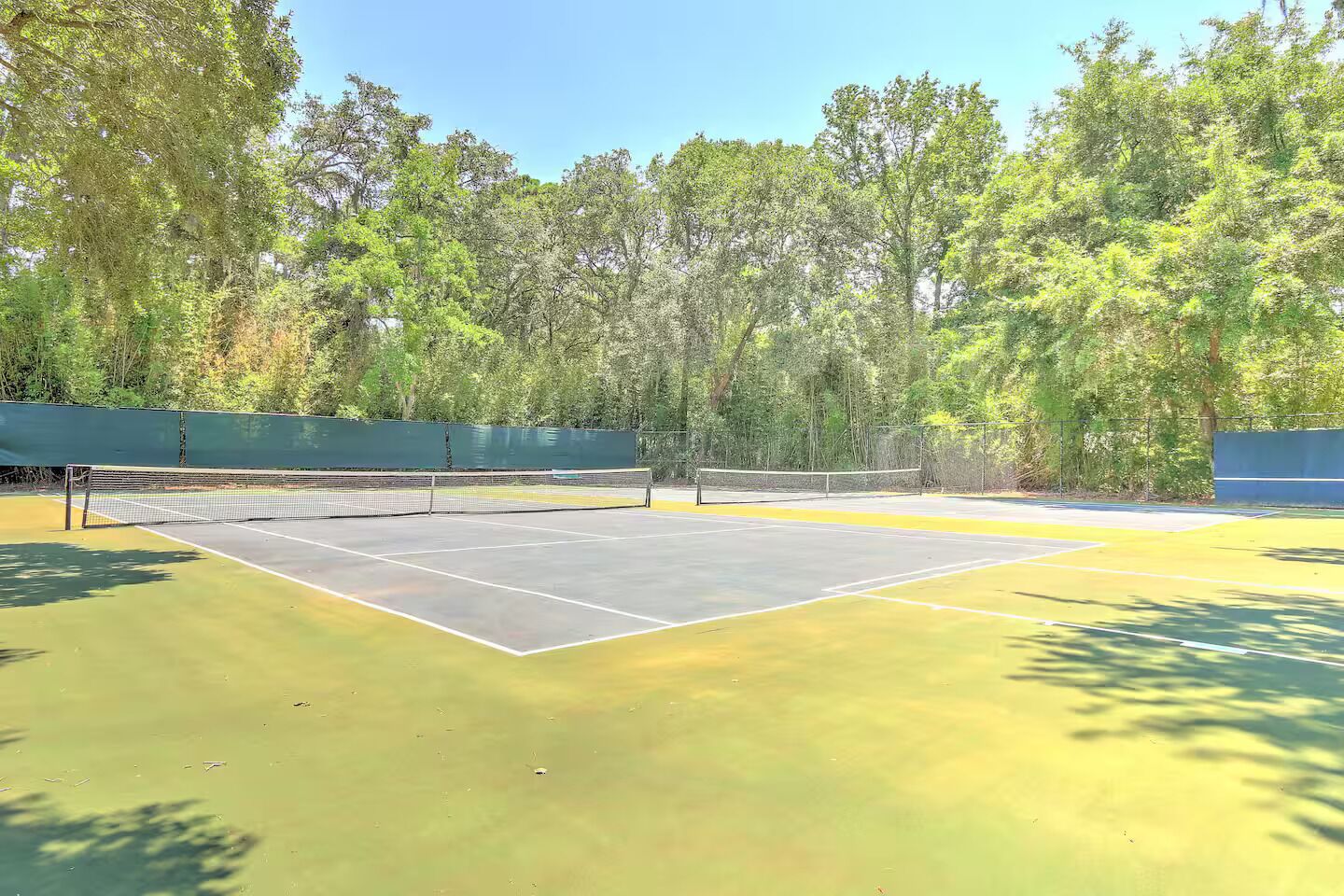 An outdoor tennis court surrounded by trees.
