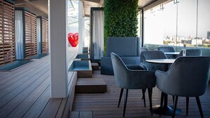 A modern outdoor seating area with wooden flooring, cushioned seating, and a green wall. - Hot Elite | Love Hotel | Solo Adultos (Mexico City)