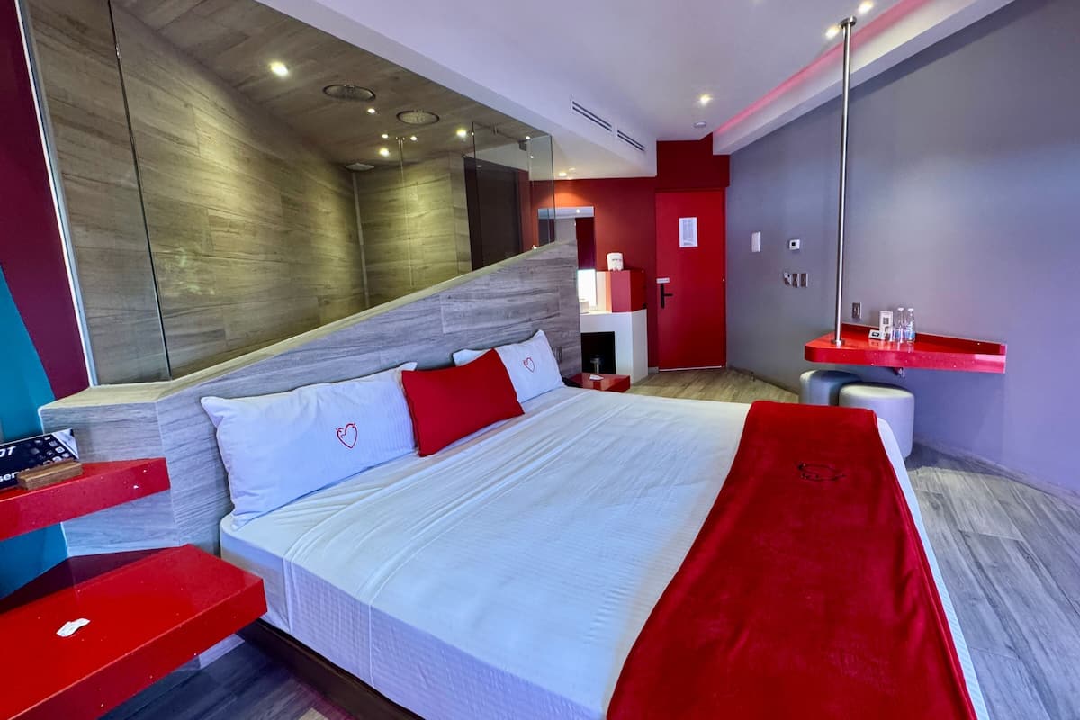 A modern hotel room with a large bed, a red accent wall, and a wooden headboard.