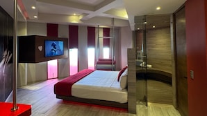 A modern hotel room with a large bed, a television, a red accent wall, and a glass partition. - Hot Elite | Love Hotel | Solo Adultos (Mexico City)