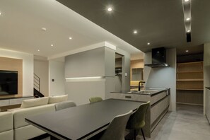 Et moderne køkken med en central ø, integrerede hårde hvidevarer og et spiseområde med sofa og stole.