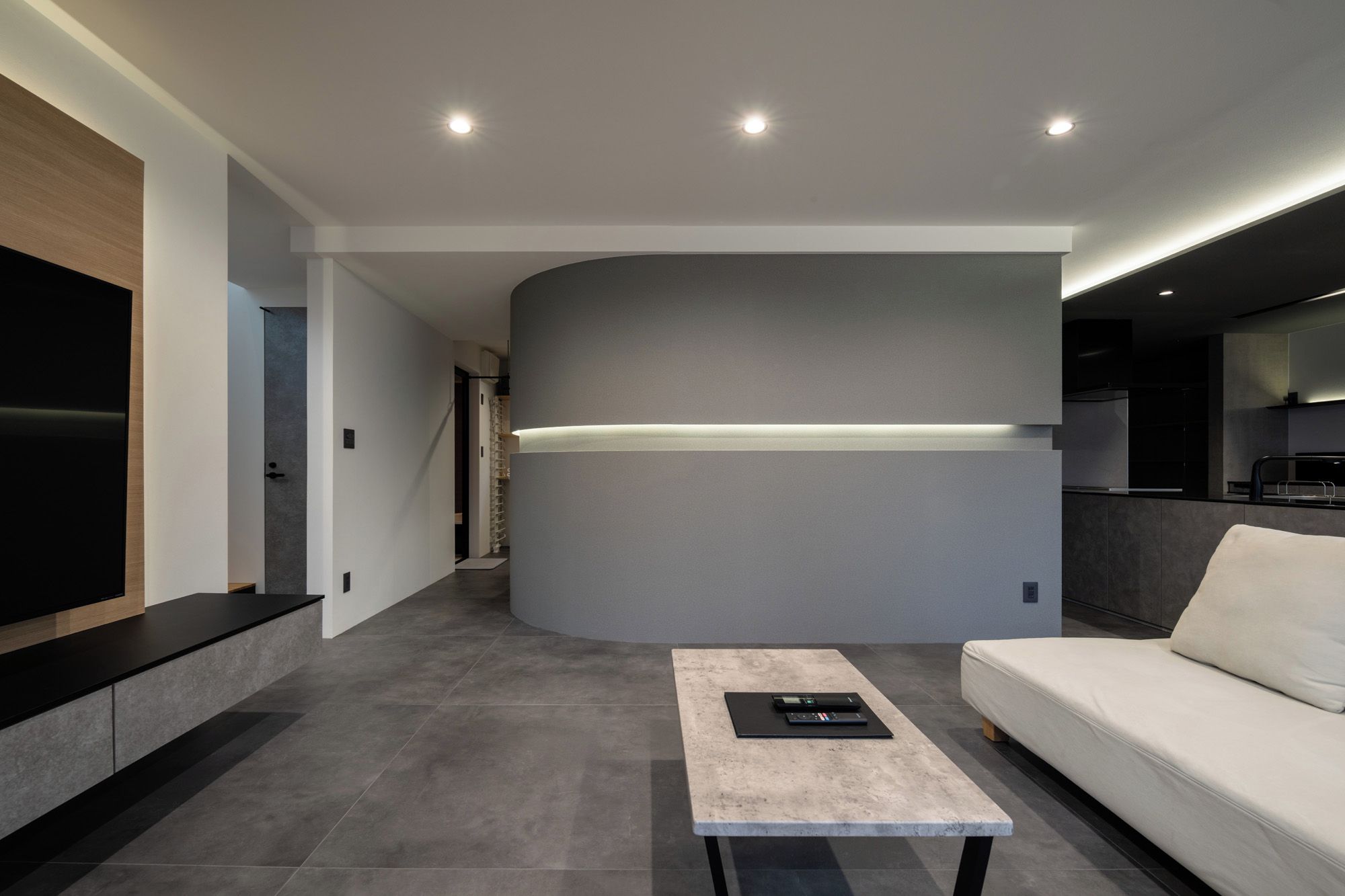 Una sala de estar moderna con un televisor de pantalla plana, un sofá, una mesa de centro y una cocina con horno empotrado.