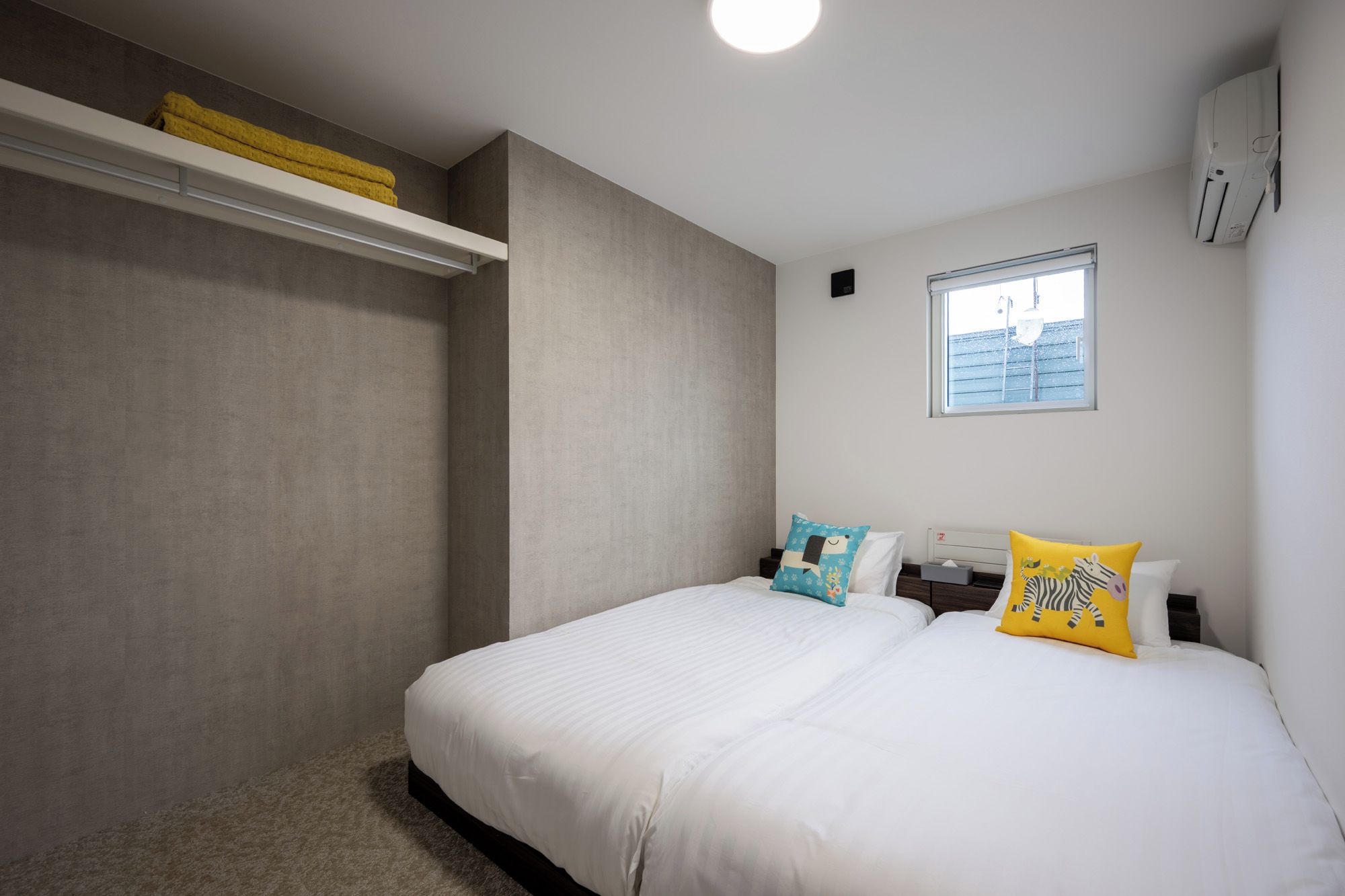 A bedroom with a bed, two pillows, a window, and a shelf with towels.