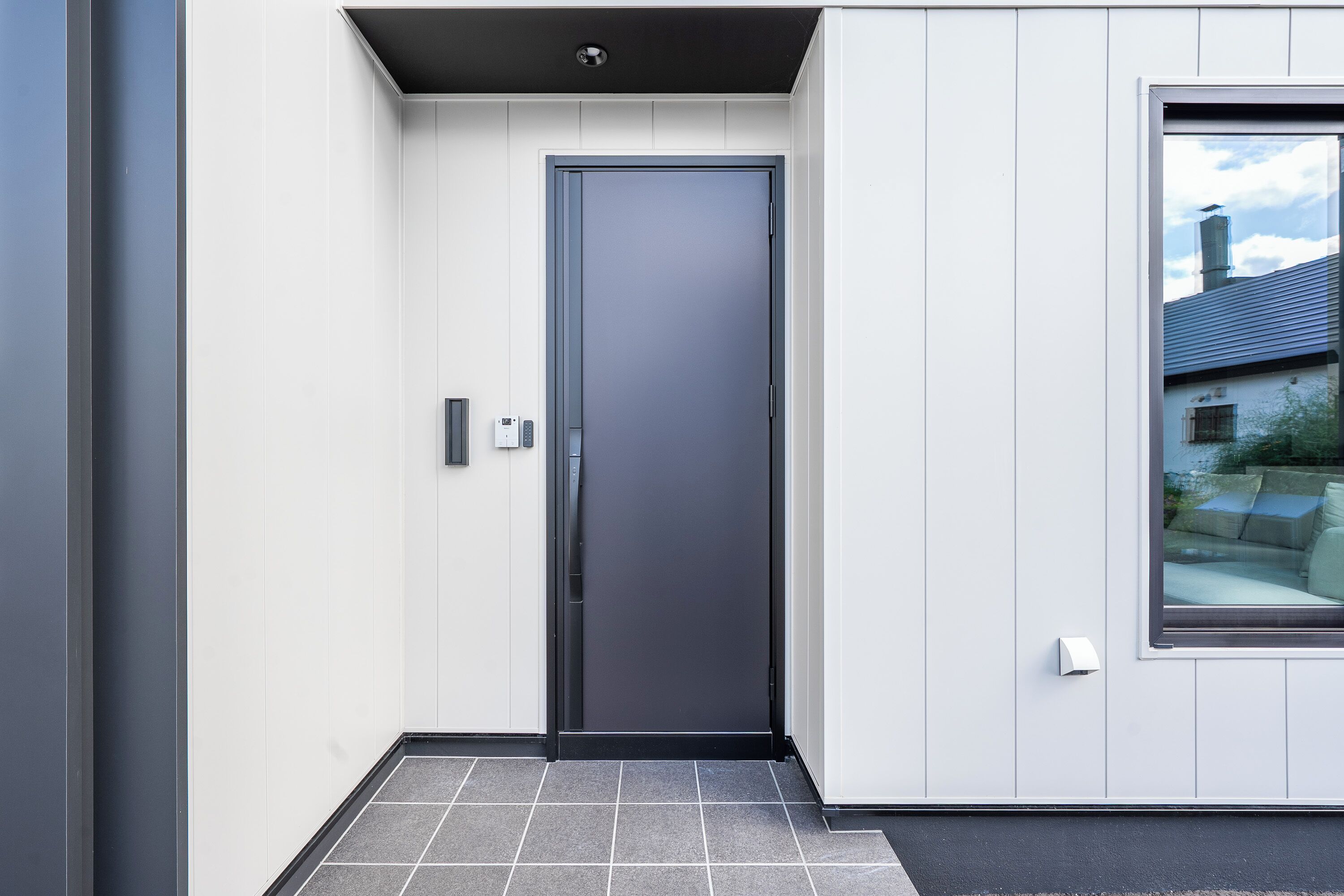 A modern exterior with a grey door, white walls, and a window.