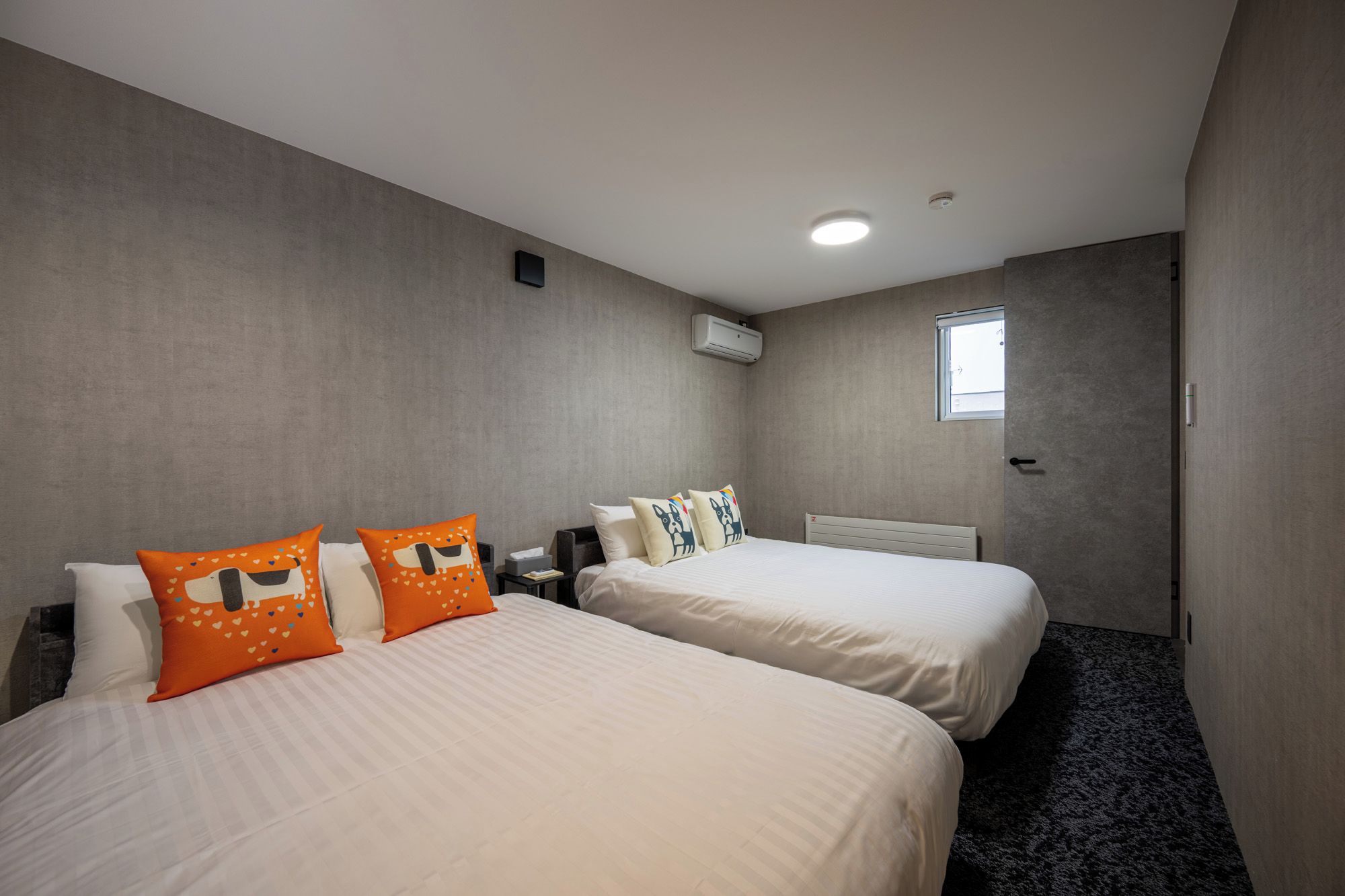 Una camera d'albergo con due letti, una finestra, un condizionatore e una porta.