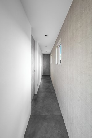 A narrow hallway with a concrete floor and walls, leading to a door at the end. - S suzukou (Asahikawa)