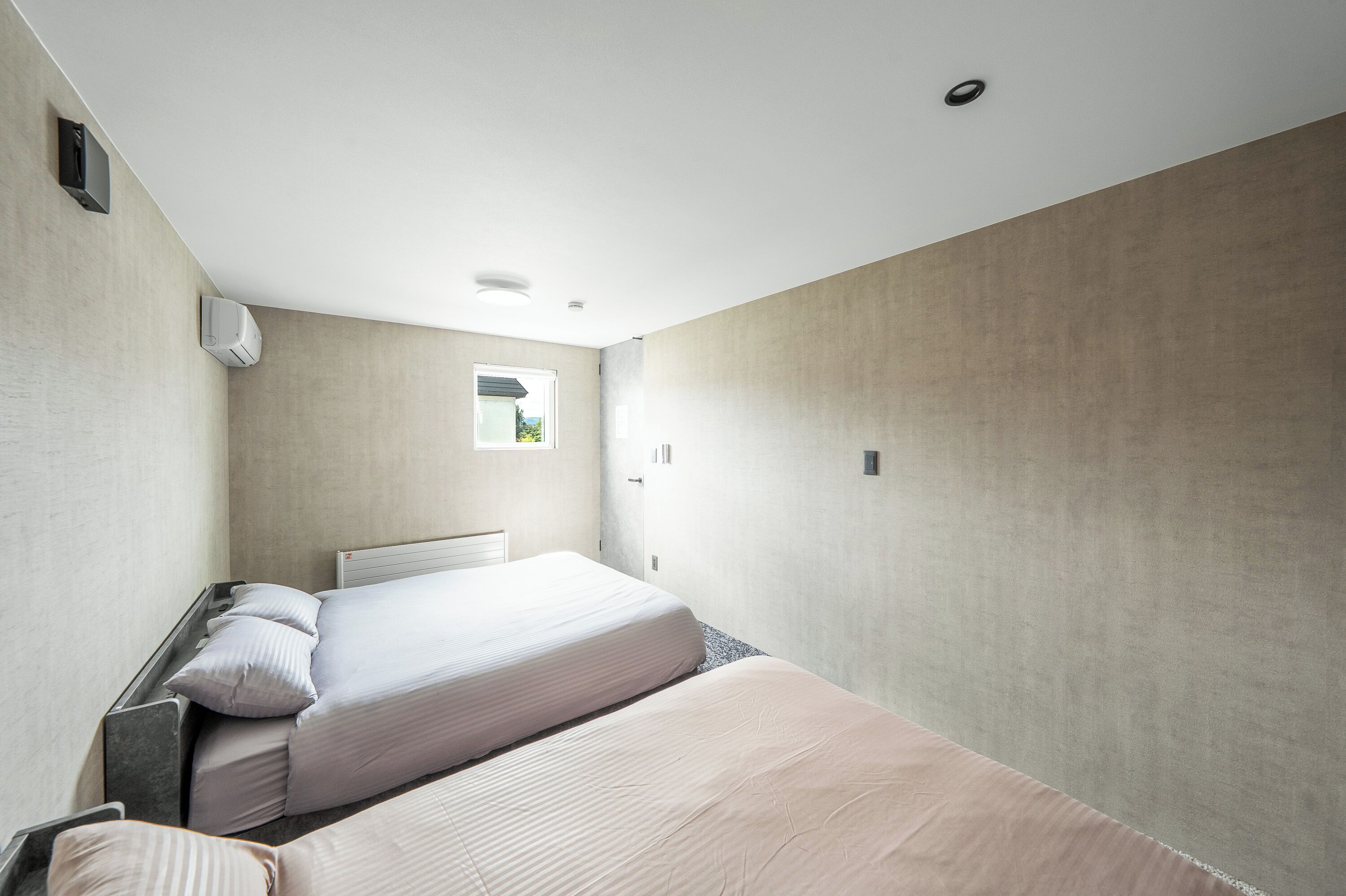 Une chambre d'hôtel moderne avec deux lits, une fenêtre et un mur uni.