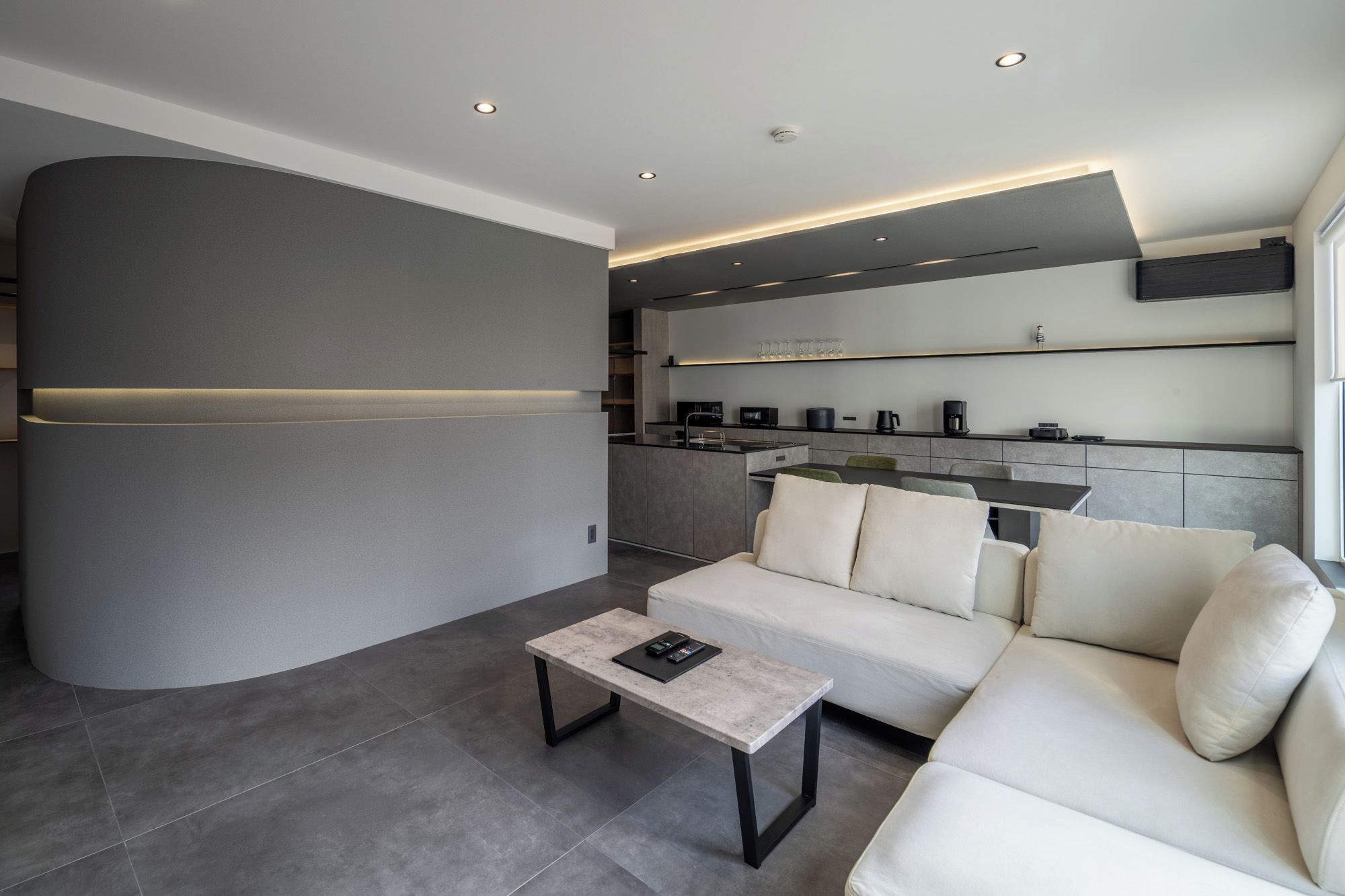 A modern living room with a sofa, a coffee table, and a kitchen area with appliances.