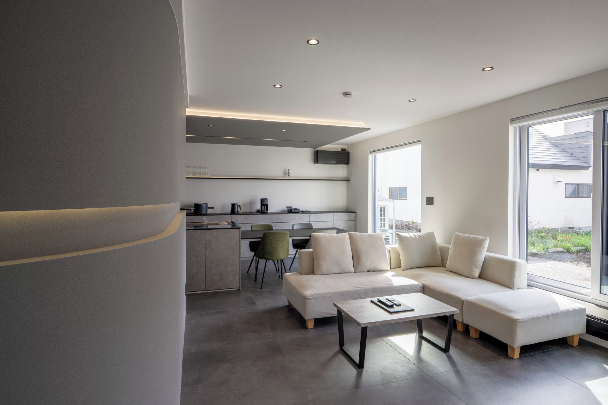 A modern living room with a sectional sofa, a coffee table, and a dining area with chairs and a kitchen in the background.