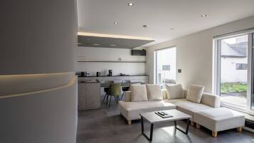 A modern living room with a sectional sofa, a coffee table, and a dining area with chairs and a kitchen in the background.