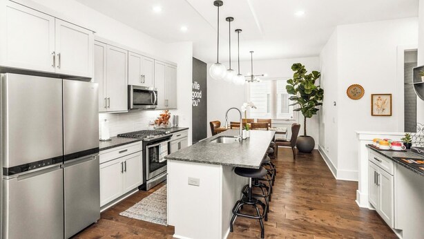 A modern kitchen with stainless steel appliances, a central island with bar stools, and a dining area with a large plant.