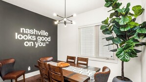 A dining area with a dark wall, a modern chandelier, and a large potted plant.