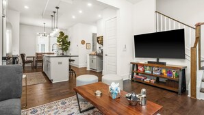 A modern living room with a wooden coffee table, a television on a wooden stand, and a kitchen in the background.