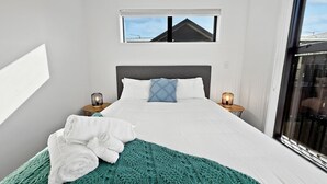A modern bedroom with a large bed, a view of the sky through a window, and a balcony. - Stylish 2BR, 2BA Retreat with Yard in Christchurch (Christchurch)