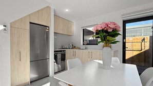 A modern kitchen with a stainless steel refrigerator, wooden cabinets, and a white dining table with chairs. - Stylish 2BR, 2BA Retreat with Yard in Christchurch (Christchurch)