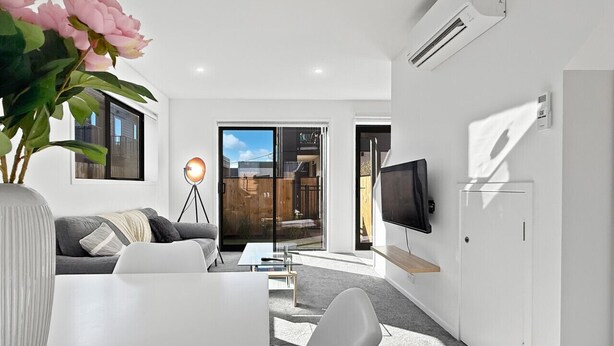 A modern living room with a white sofa, a dining table, and a large window. - Stylish 2BR, 2BA Retreat with Yard in Christchurch (Christchurch)