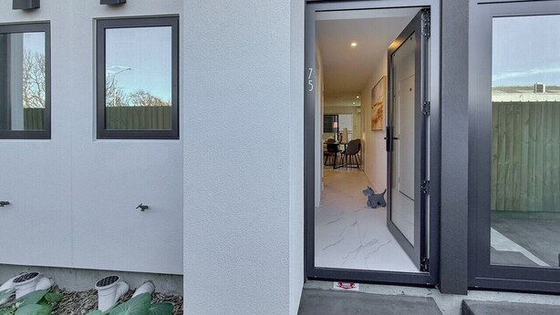 Un bâtiment moderne à la façade grise, une porte donnant sur un espace intérieur et le chiffre « 75 » bien visible sur le mur.