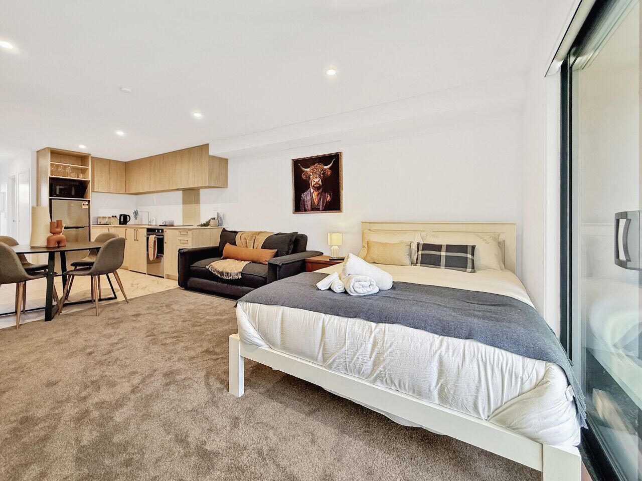 Ein modernes Hotelzimmer mit Bett, Sofa, Esstisch und Küchenzeile.