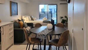 En modern lägenhet med ett matområde, en soffa, en säng och utsikt över staden genom stora fönster.