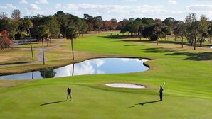 Un parcours de golf avec un étang, des arbres et un ciel dégagé.