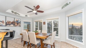 A dining area with a wooden table and chairs, a ceiling fan, and large windows with a view of trees and mountains. - 4,000 SF Luxury Home | 6-BR + 5-BA | 2-minute DRIVE to Jasper National Park (Jasper)