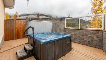 Ein Whirlpool auf einer Holzterrasse mit einer Steinmauer und einem Fenster mit Blick auf ein bewaldetes Gebiet.