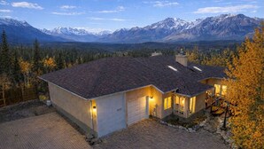 A two-story house with a sloped roof, a garage, and a driveway. It is surrounded by a forest and mountains in the background. - 4,000 SF Luxury Home | 6-BR + 5-BA | 2-minute DRIVE to Jasper National Park (Jasper)