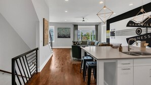A modern kitchen with a large island, a dining area with a sofa, and a view of the outside. - Vibrant 12 Bed Oasis! Luxury meets spacious! Full Kitchen with Huge Rooftop! (Nashville)