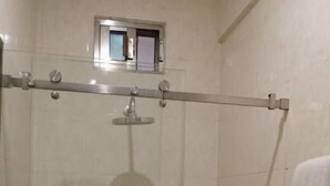Cabina de ducha con paredes de vidrio, un cabezal de ducha manual, una ventana pequeña y una toalla colgada en la pared.