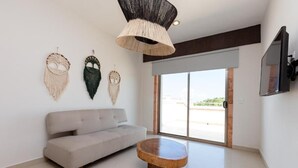 Una sala moderna con un sofá, una mesa redonda de madera y tres colgadores de macramé en la pared.