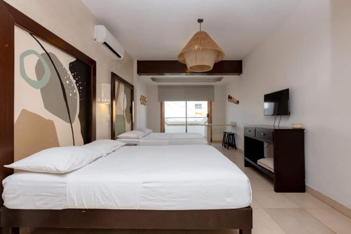 Un dormitorio con dos camas, un escritorio, un televisor y un ventanal amplio.