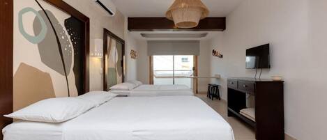 A bedroom with two beds, a desk, a television, and a large window.