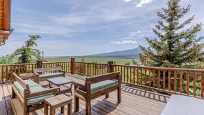 Eine Holzterrasse mit Gartenmöbeln, Blick auf einen Berg und einen Wald im Hintergrund.