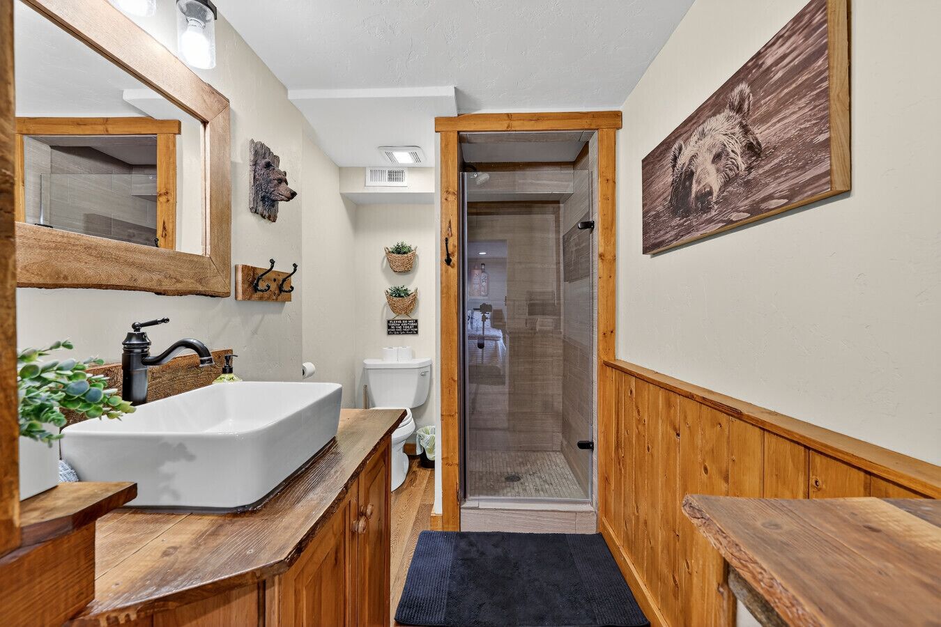 A bathroom with a wooden vanity, a large mirror, a white sink, and a shower area.