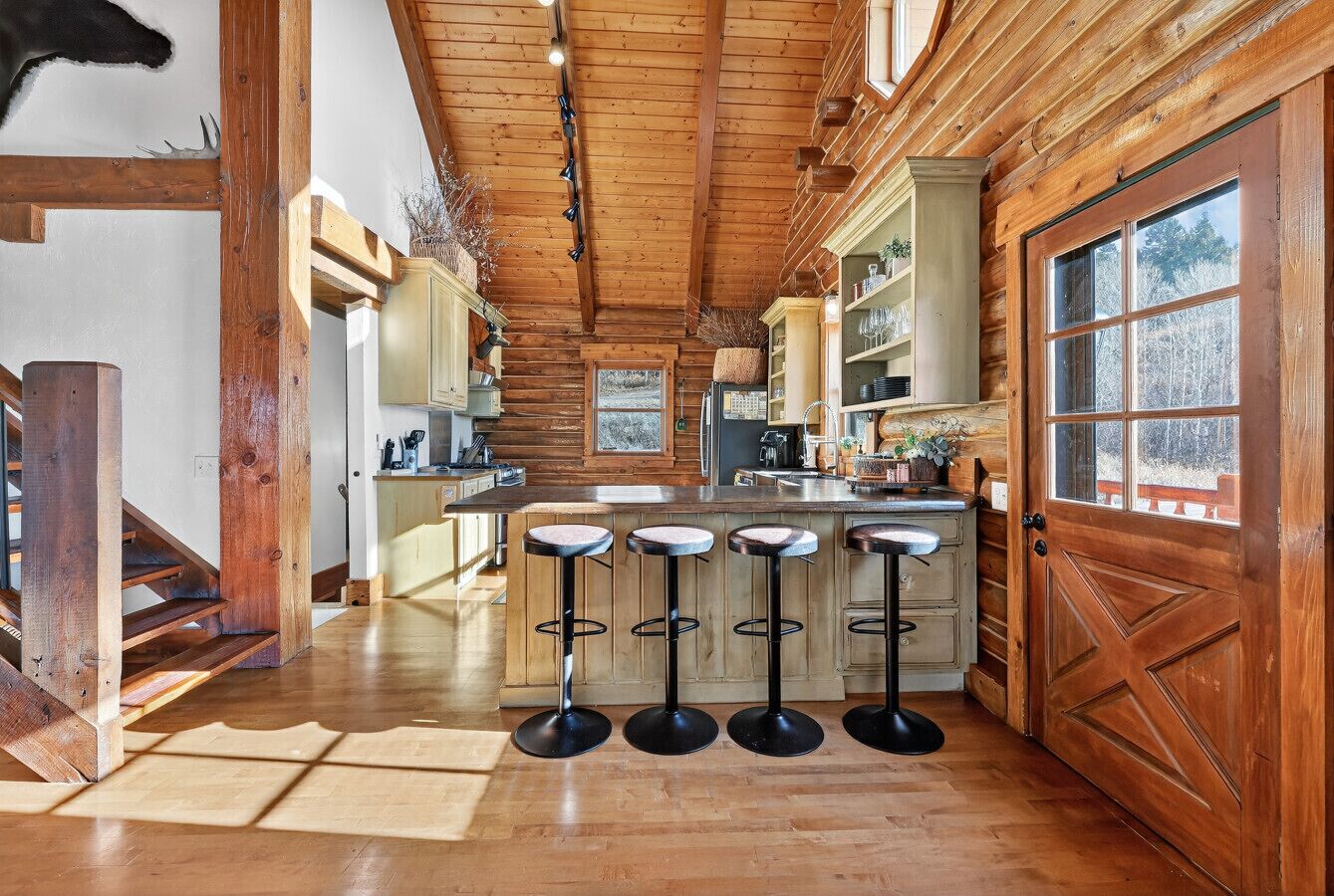 A spacious kitchen with wooden beams, a central island with stools, and a large wooden door.