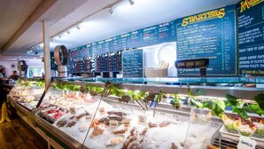 Un présentoir de fruits de mer avec différents types de poissons et de crustacés, un tableau affichant les entrées et les plats du jour, et un comptoir avec une caisse enregistreuse.