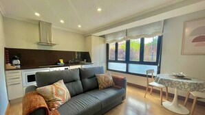 A modern living room with a grey sofa, a dining table with chairs, and a kitchen in the background. - Okai Etxea Bermeo, suite in the center of the town (Bermeo)