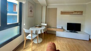 A compact living space with a dining table, chairs, a sofa, a TV, and a window with blinds. - Okai Etxea Bermeo, suite in the center of the town (Bermeo)