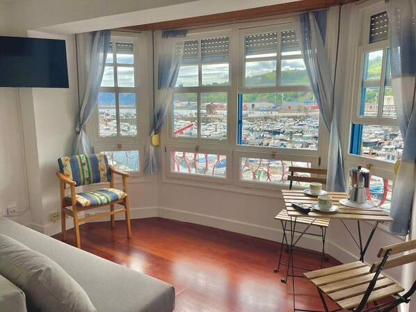 A room with a wooden floor, a sofa, a chair, a table with a coffee pot, and a TV. - Portu Suite , en el mismo puerto (Bermeo)