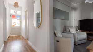 A hallway with wooden flooring and a door leading to a room with a grey sofa, a flat-screen TV, and a wall-mounted mirror. - South Launceston Gem, Minutes to Cataract Gorge (Launceston City)