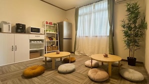 Een gezellige kamer met twee ronde tafels, een boekenkast, een koelkast en een potplant.